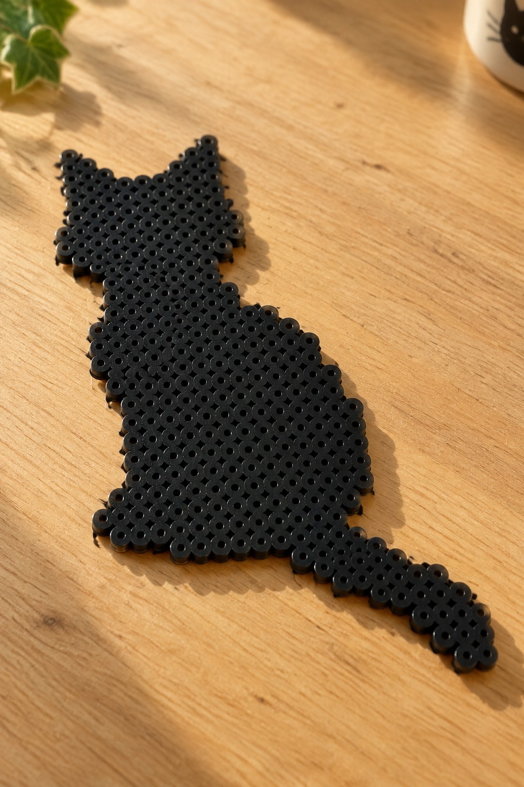 Black perler bead cat figure on light wooden table with extended tail