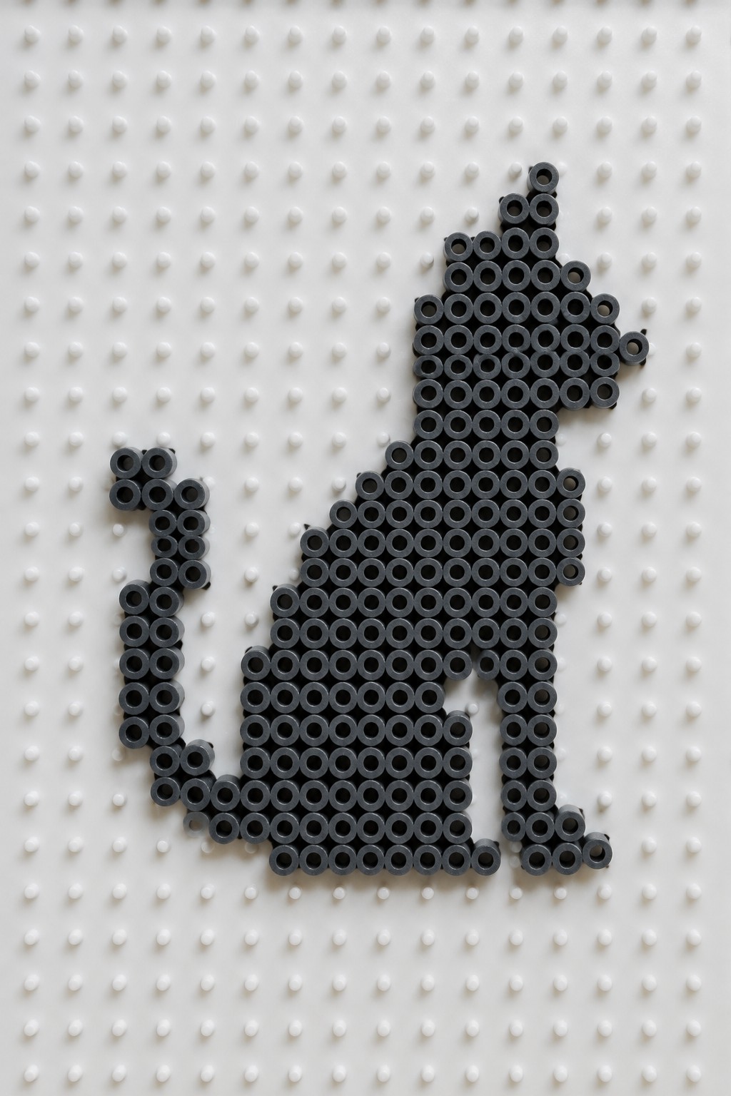 Black beads form a sitting cat silhouette on white pegboard with holes