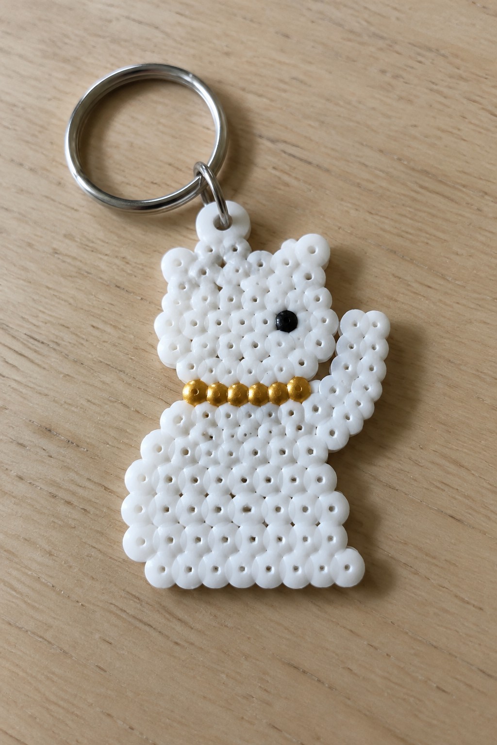 White beaded cat keychain with gold collar, black eye, silver ring on wood
