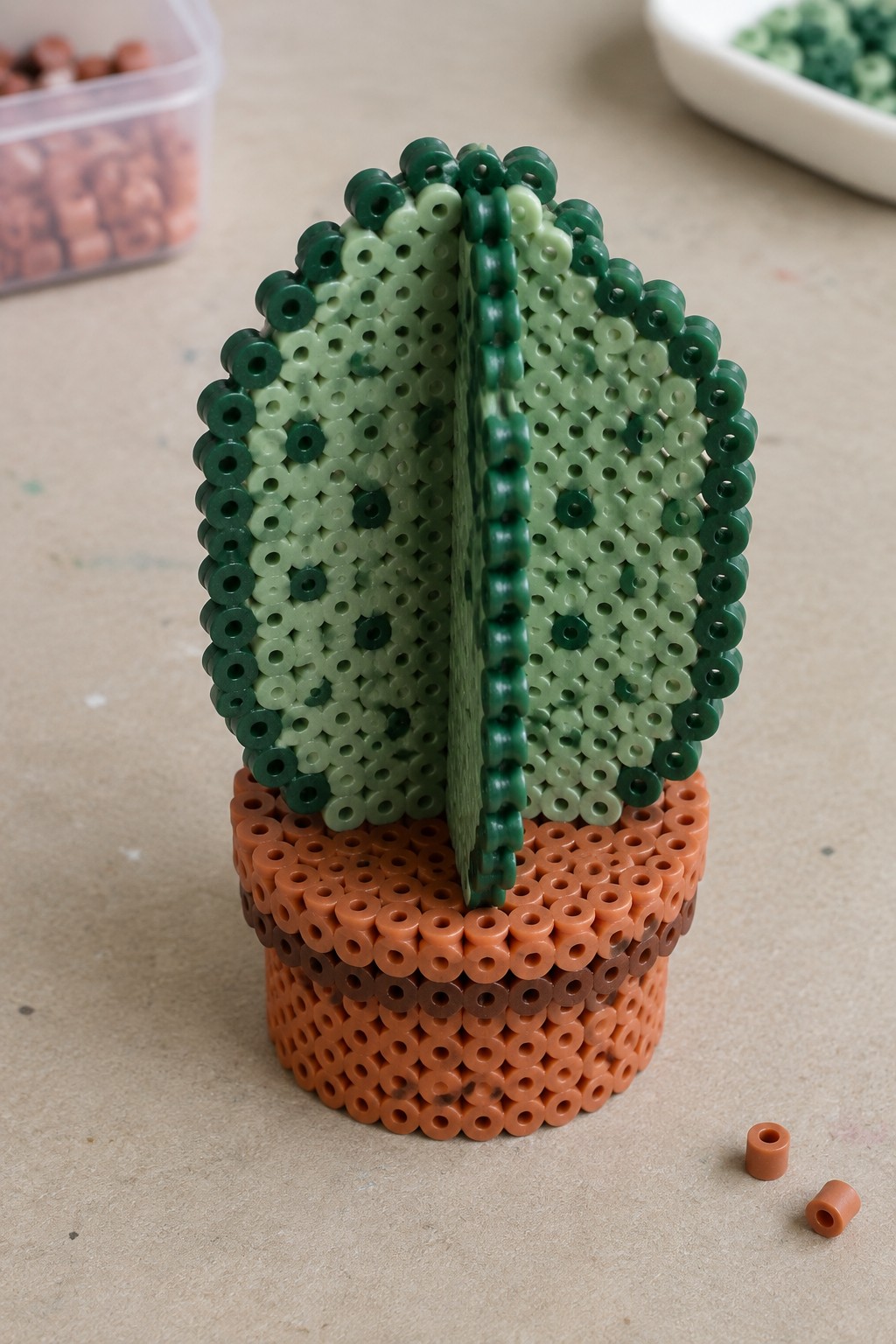 Green perler bead cactus in orange-brown pot with loose beads nearby