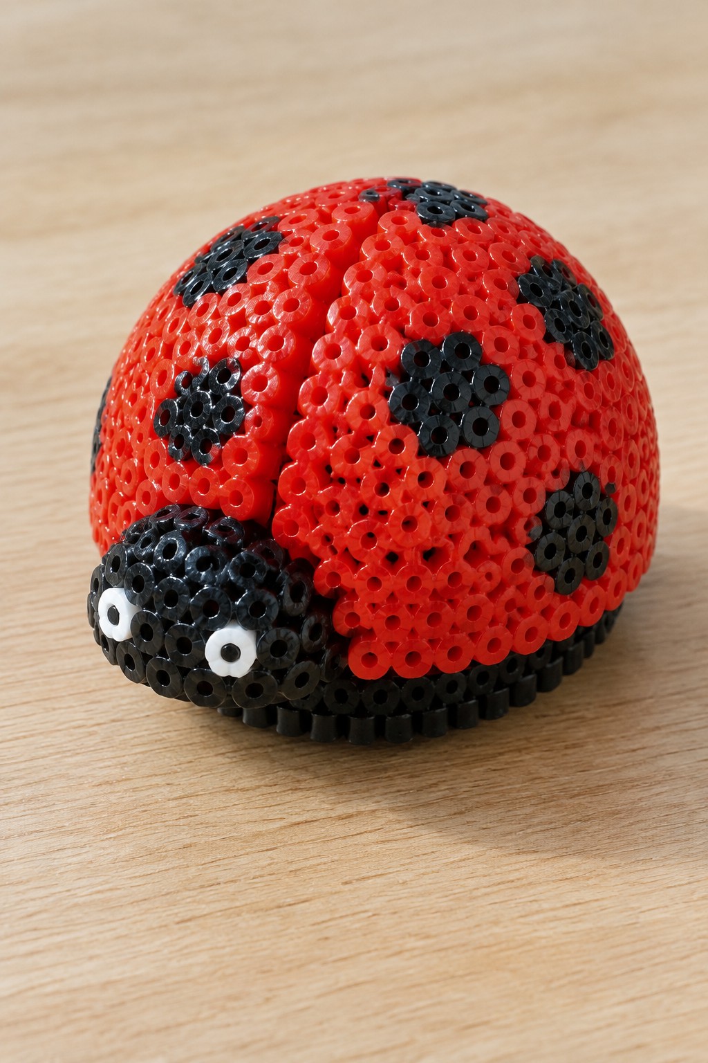 Red beaded ladybug with black spots and eyes on wooden surface