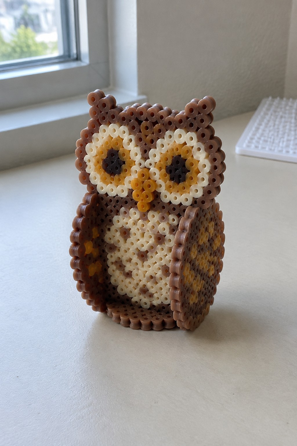 Brown perler bead owl with yellow accents on white table by window
