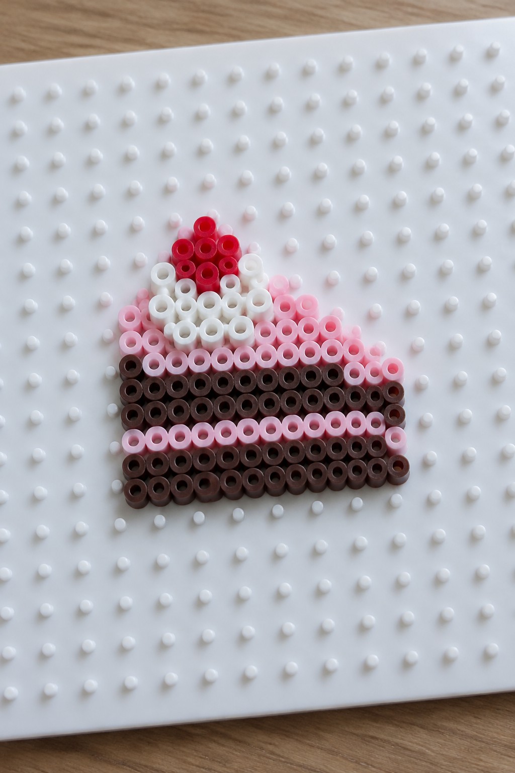 Pink and brown perler beads forming cake slice on white pegboard