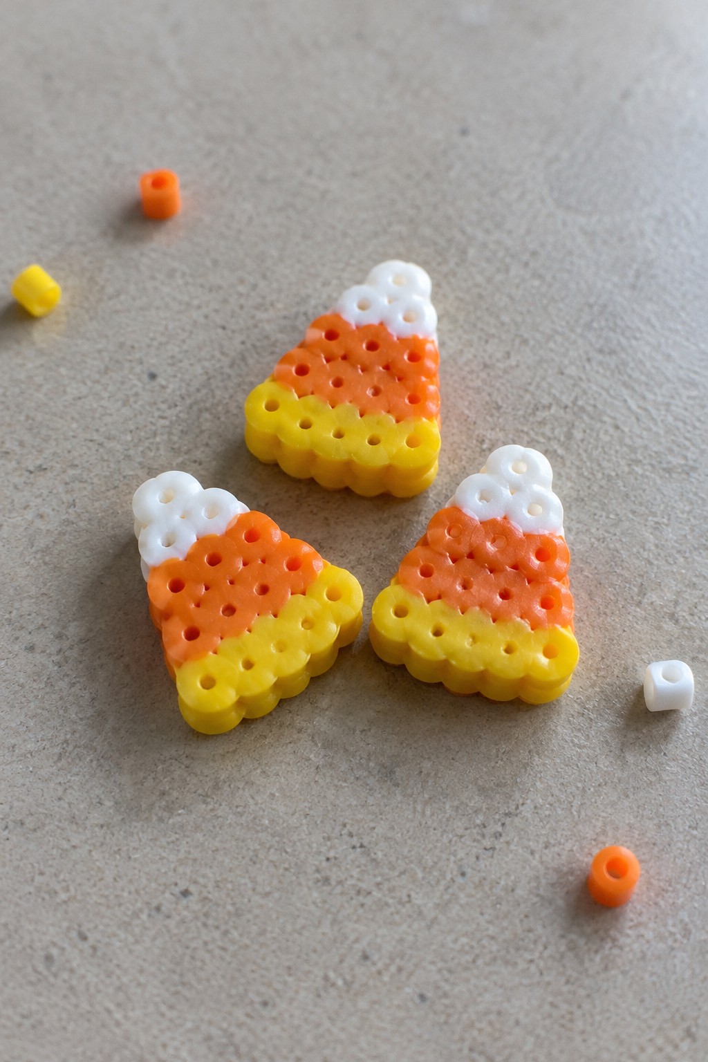 Three Perler bead candy corns in yellow, orange, and white with loose beads nearby