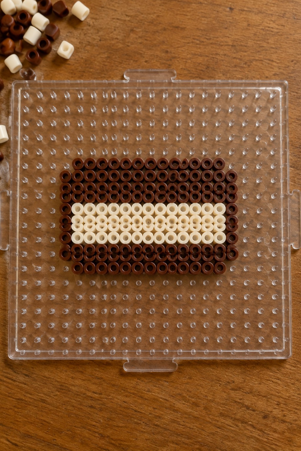 Brown and white perler beads forming a striped rectangle on clear pegboard