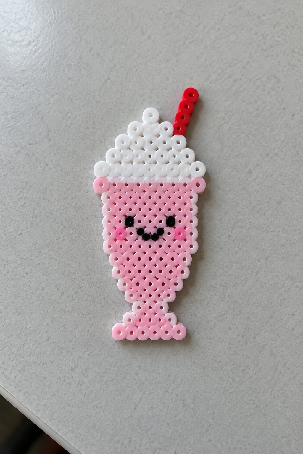 Pink perler bead milkshake with kawaii face, white topping, and red straw.