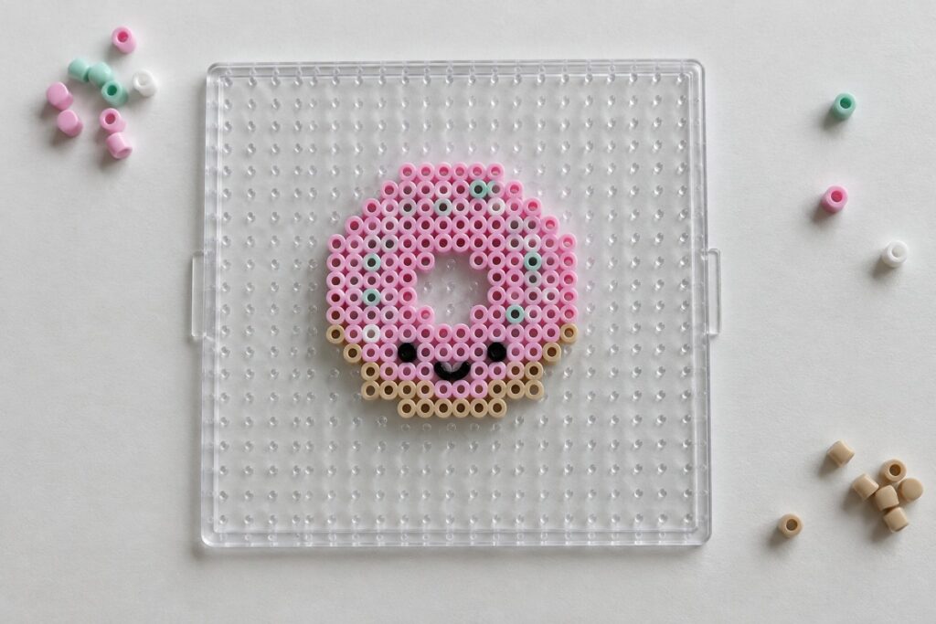 Pink perler bead face design on clear pegboard with scattered loose beads