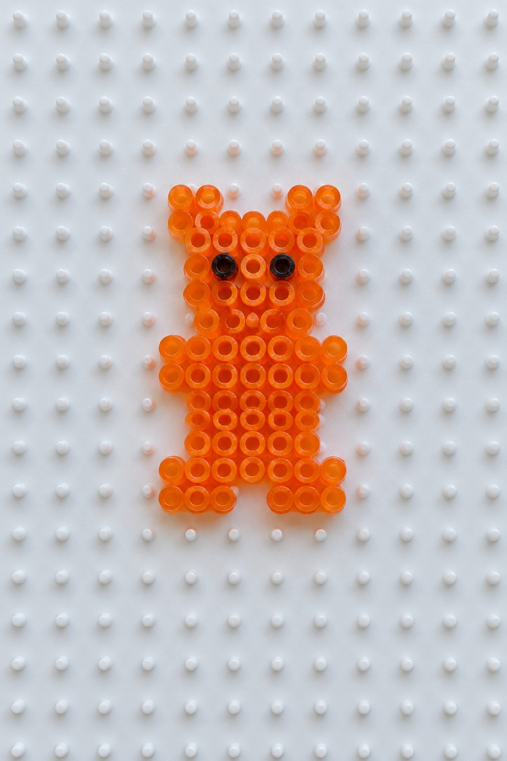 Orange perler bead bear with black eyes on white pegboard