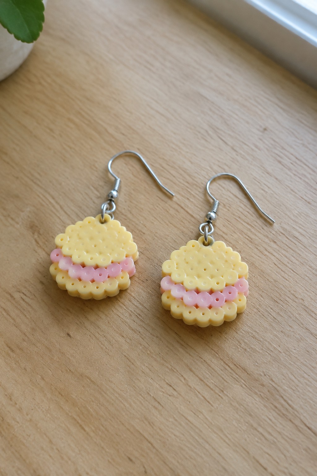 Pair of yellow and pink perler bead cake earrings on wooden surface