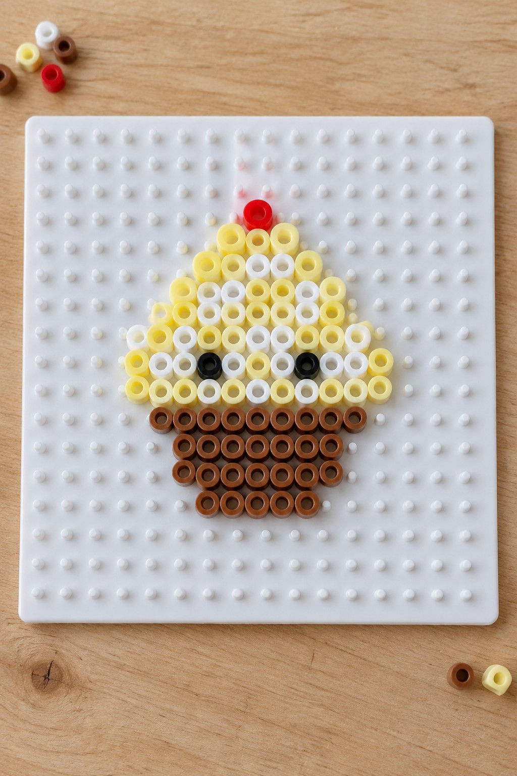 Cupcake made of yellow, white, and brown Perler beads on white pegboard.