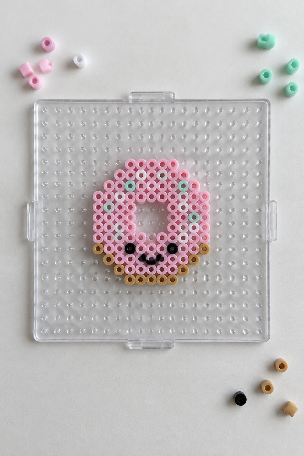 Pink perler bead face design on clear pegboard with scattered loose beads