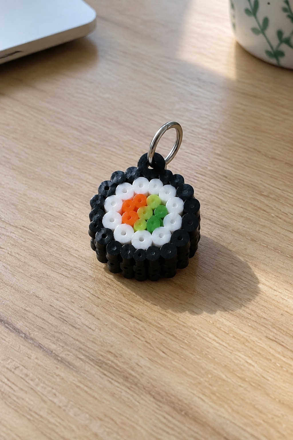 Perler bead sushi keychain with black nori, white rice, and colorful center on wood.