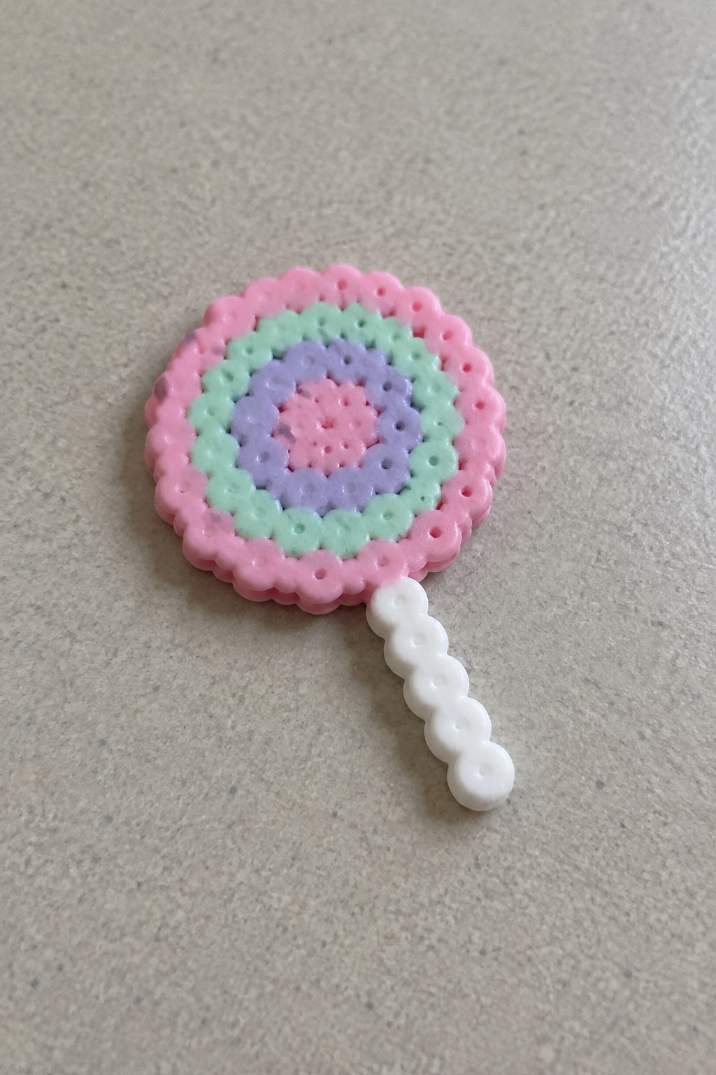 Perler bead lollipop with pink scalloped edge, green purple pink rings, white handle