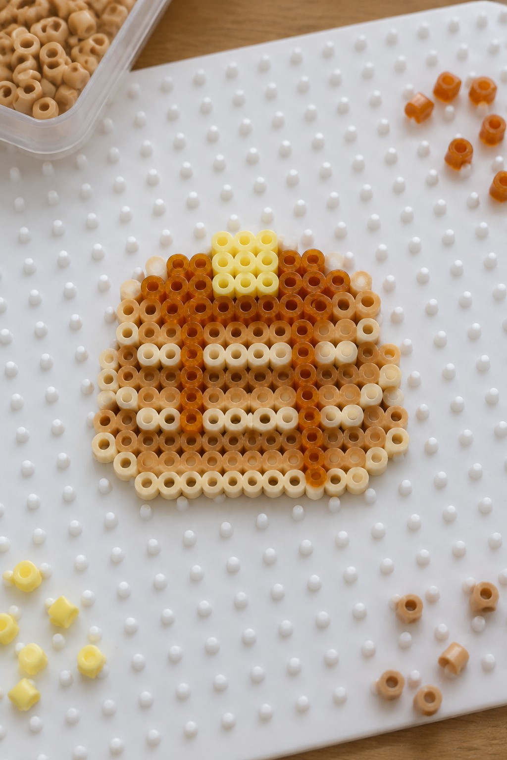 Perler beads in gradient oranges and yellow forming a pumpkin on white pegboard.