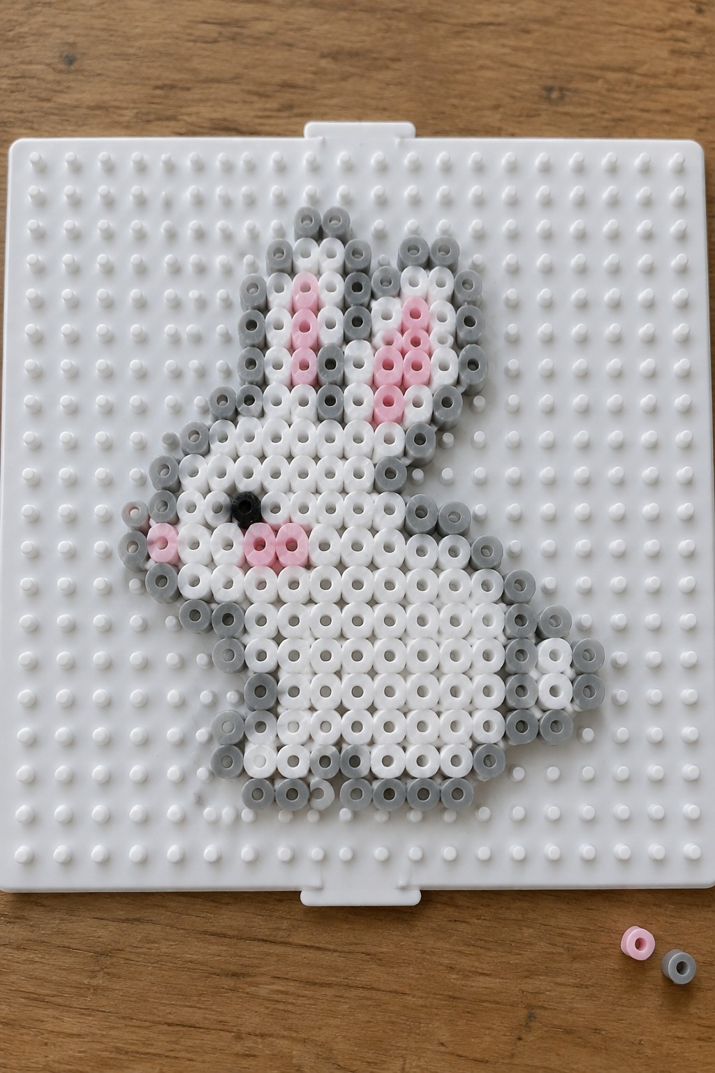 Gray and white perler bead bunny with pink accents on pegboard