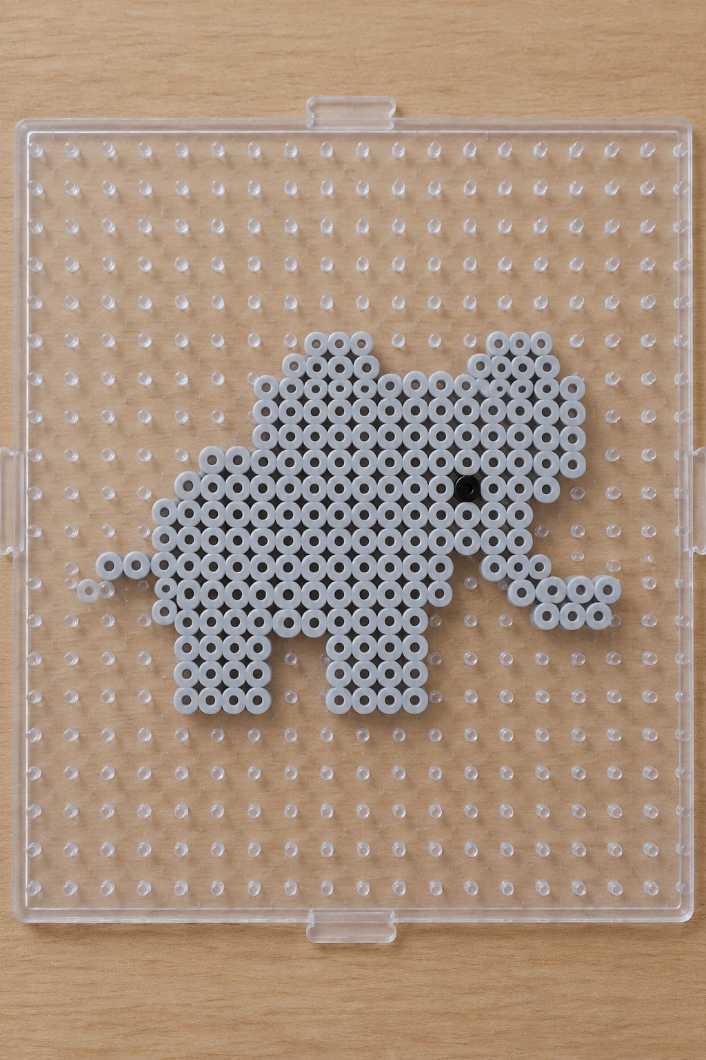 White beads form elephant shape with black eye on clear pegboard over wood