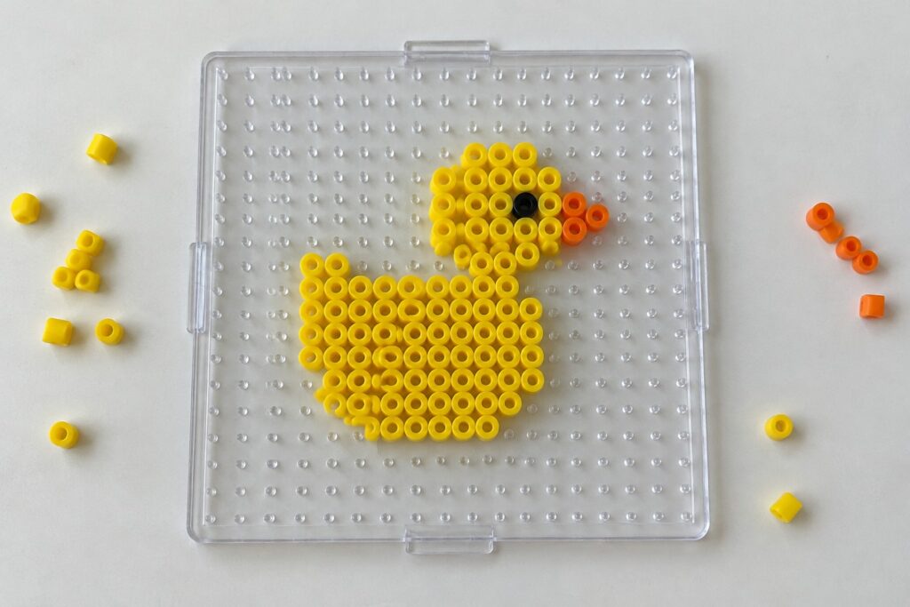 20 Easy Perler Bead Patterns for Beginner Animal Projects Yellow perler bead duck with black eye and orange beak on clear pegboard
