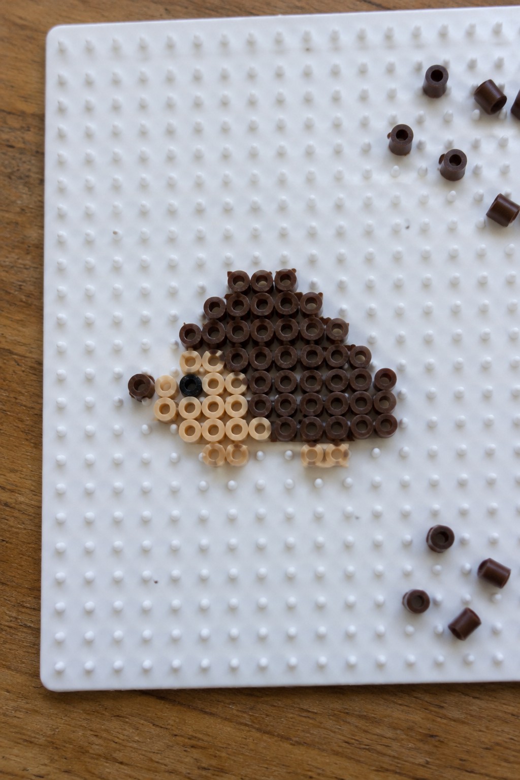 A hedgehog shape made from dark brown, light tan, and black Perler beads arranged on a white pegboard.