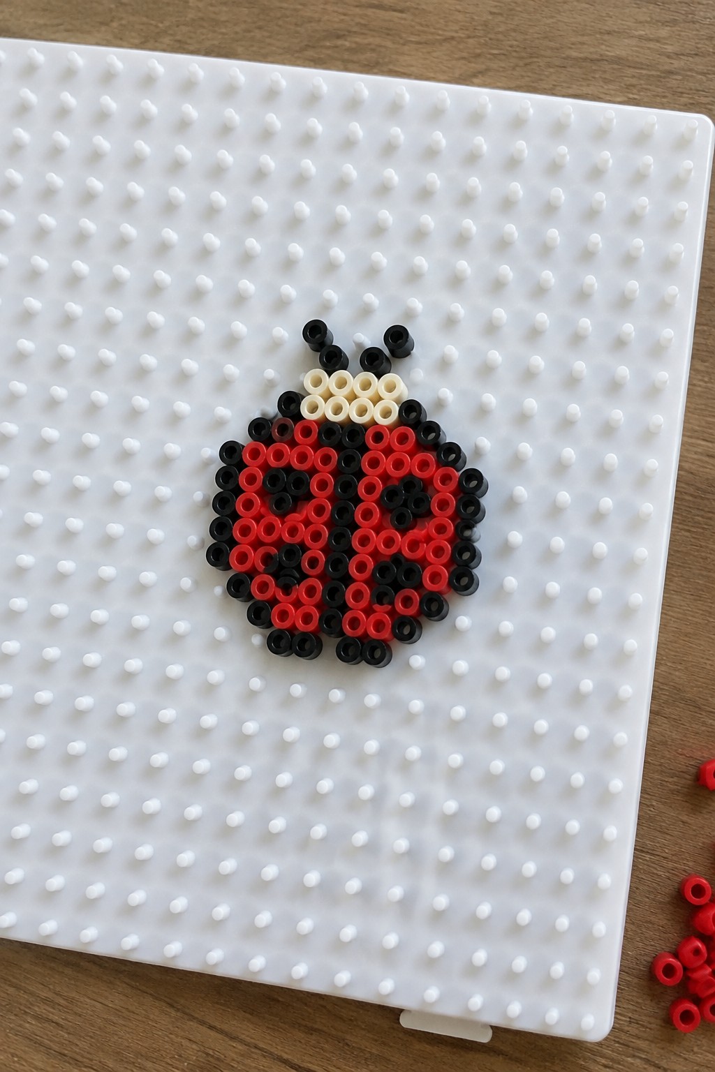 Red and black perler bead ladybug with antennae on white pegboard