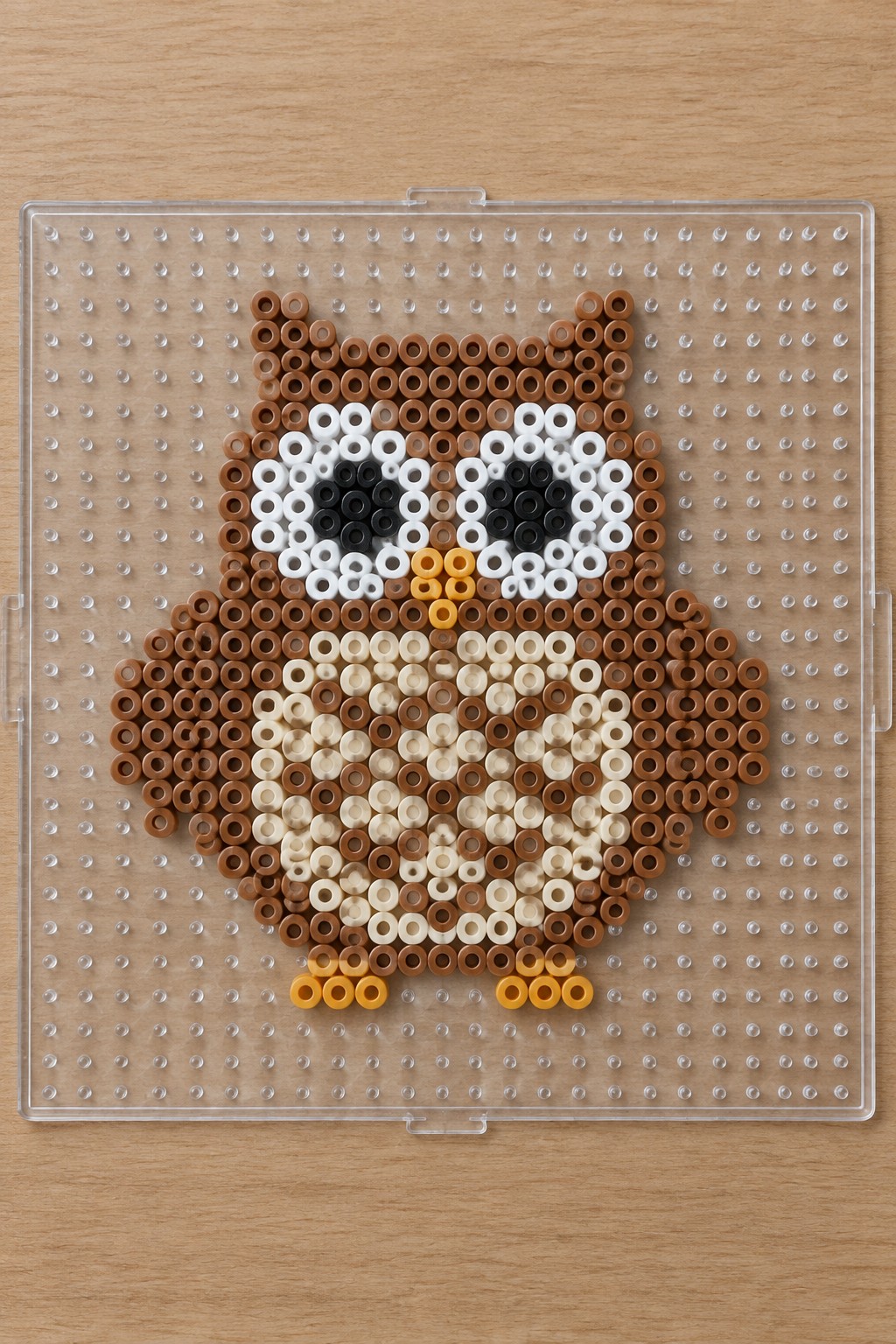 Owl made from brown, white, black, beige, and yellow perler beads on pegboard