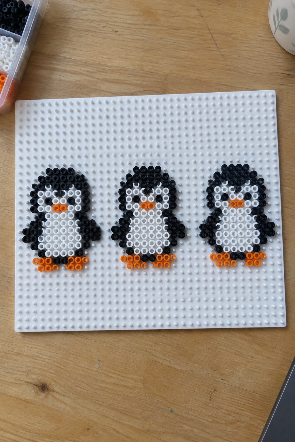 Three black, white, and orange perler bead penguins on a white pegboard.