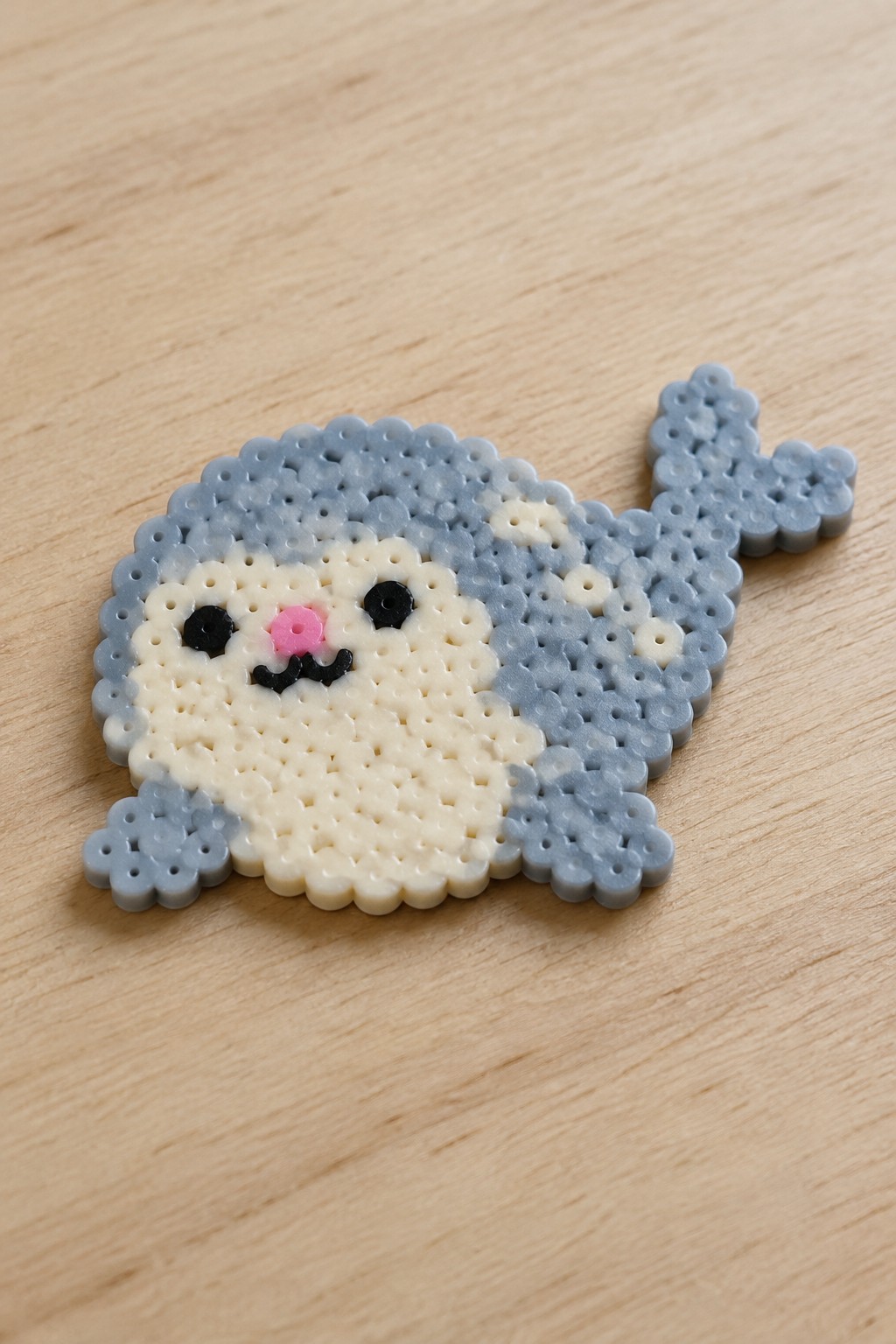 Blue and white perler bead seal with pink nose on wooden surface