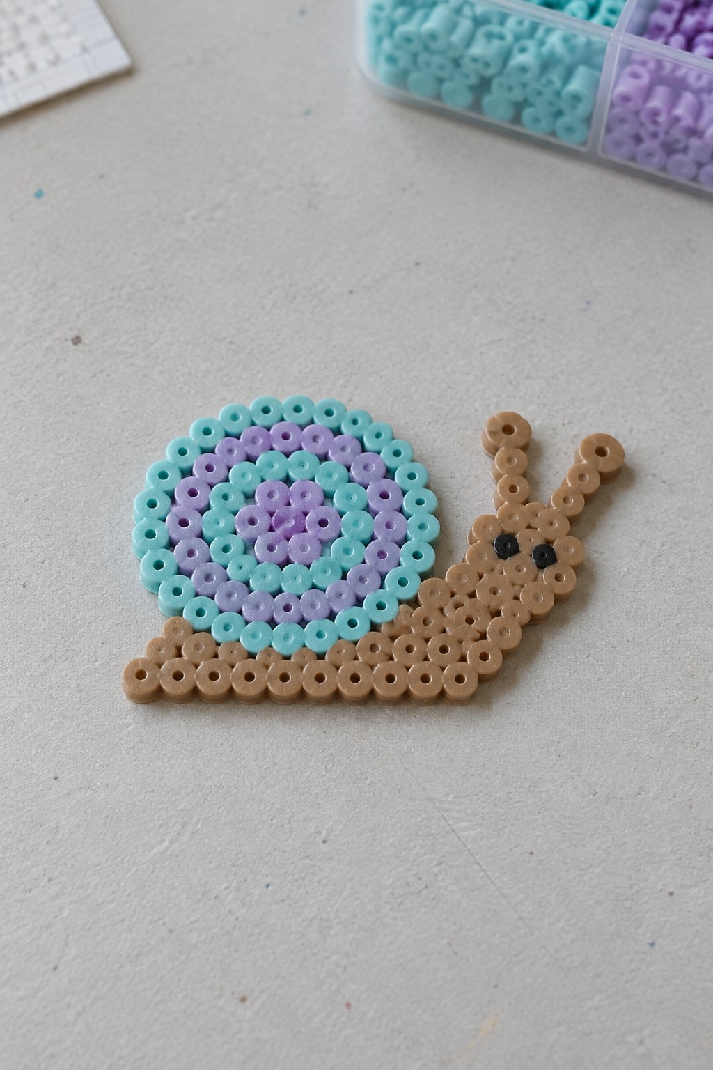 Perler bead snail with spiral cyan purple shell and brown body on table
