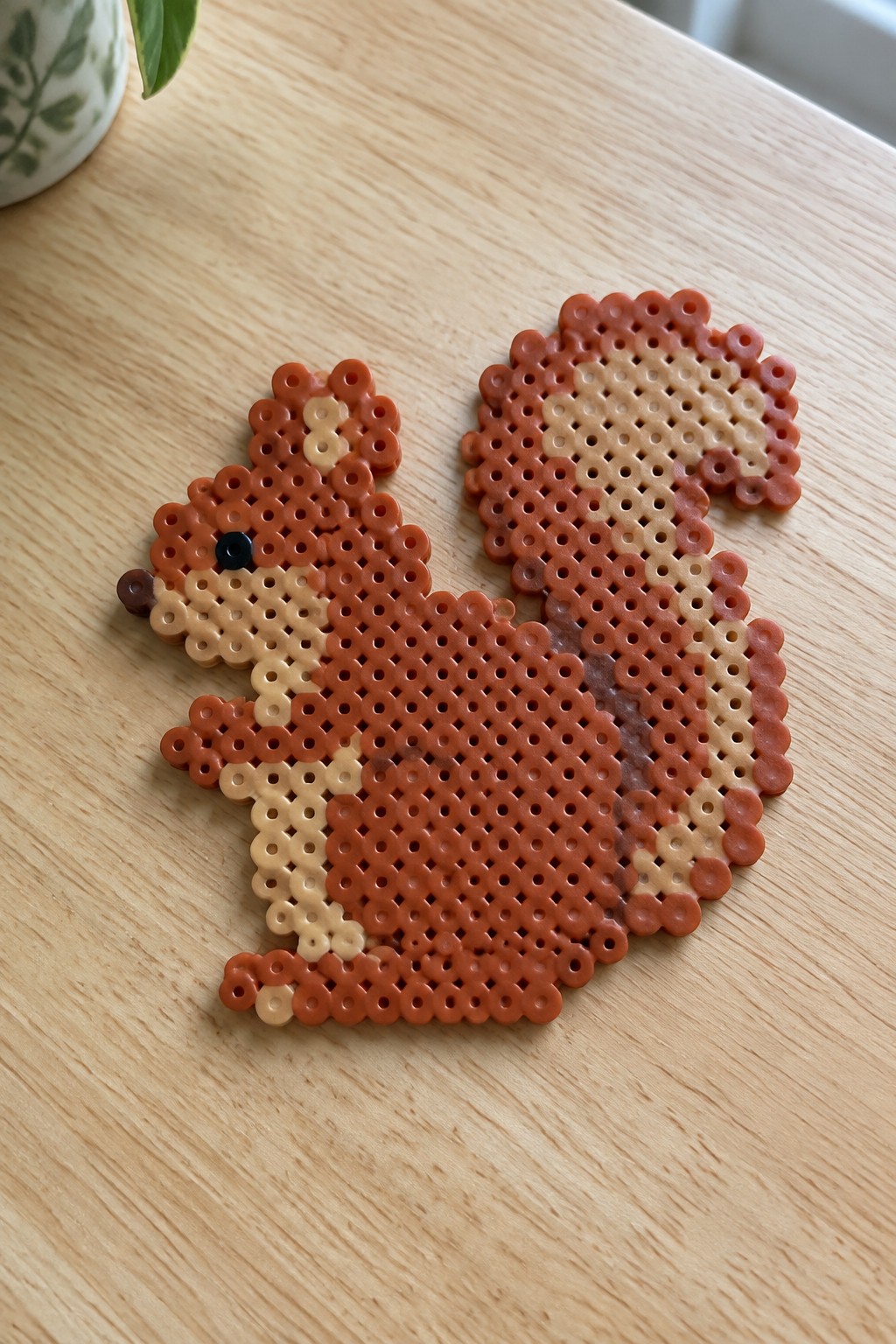 Unfused Perler beads form a squirrel with brown, orange, and beige shading on a pegboard.