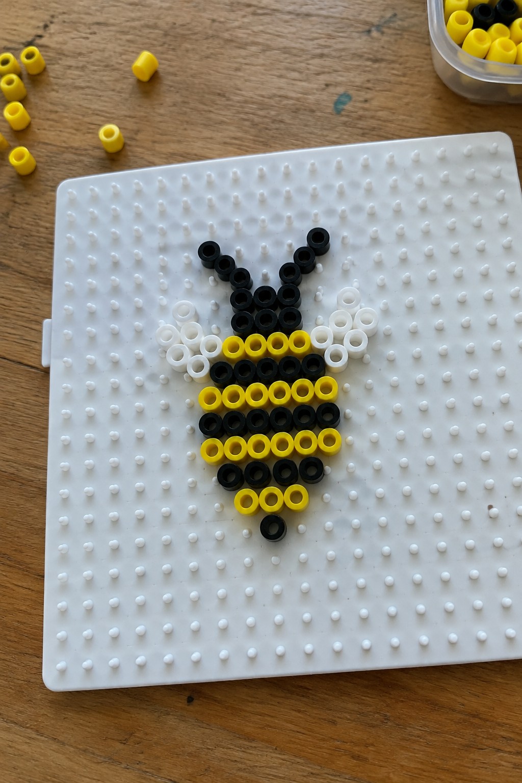 Perler bead bee pattern on a pegboard using black, yellow, and white beads.