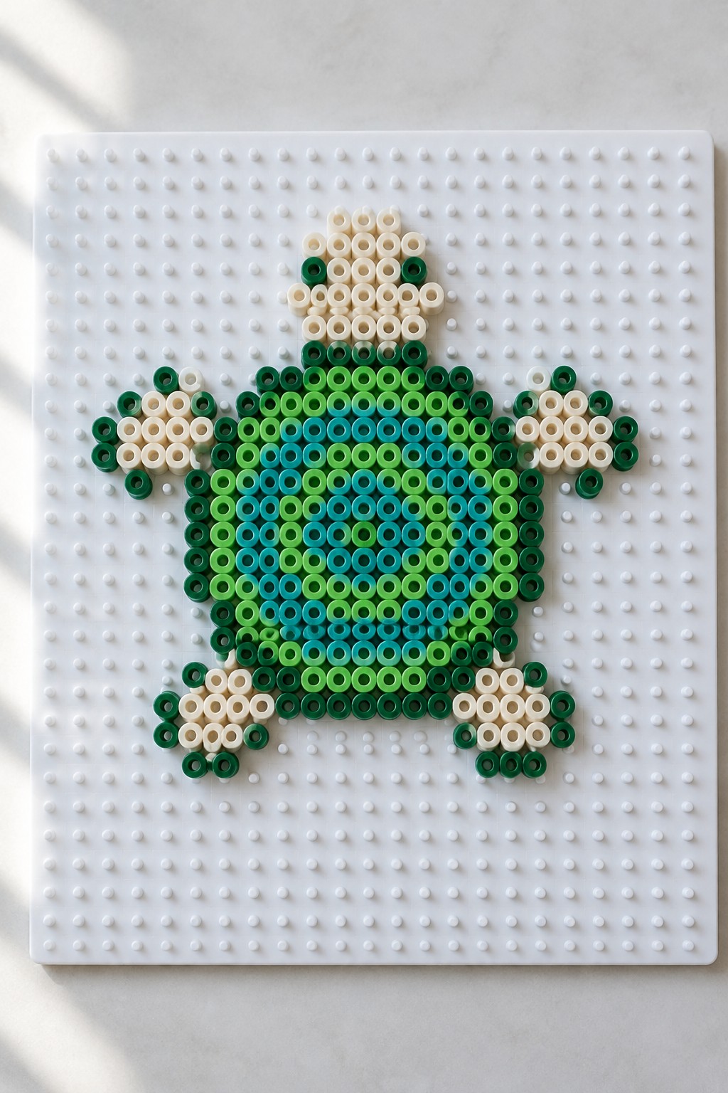 Perler bead turtle design in greens, blues, and cream on a white pegboard.