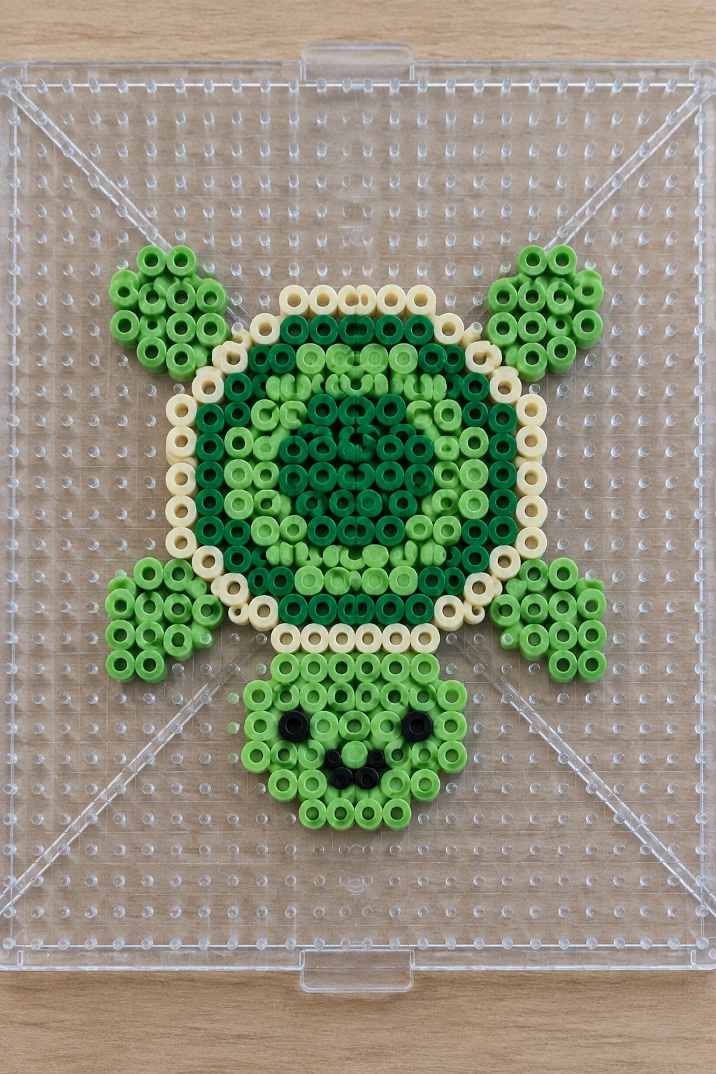 Green perler bead Yoda with beige accents on clear pegboard
