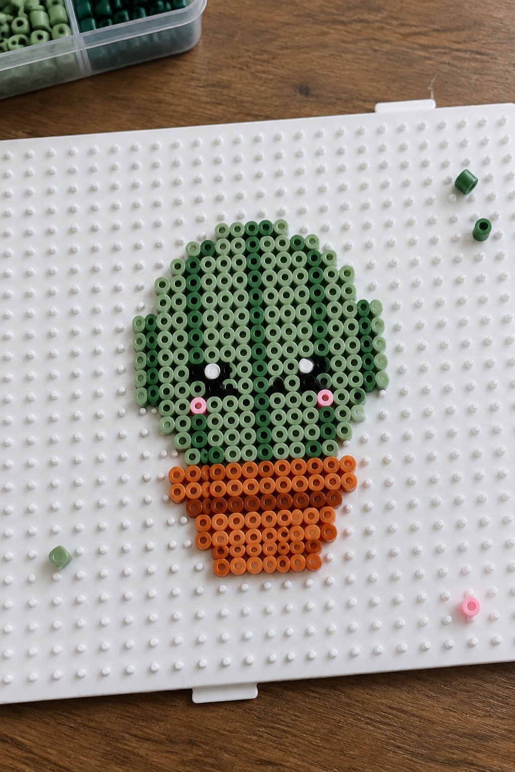 Perler beads forming a cute cactus with face in orange pot on pegboard