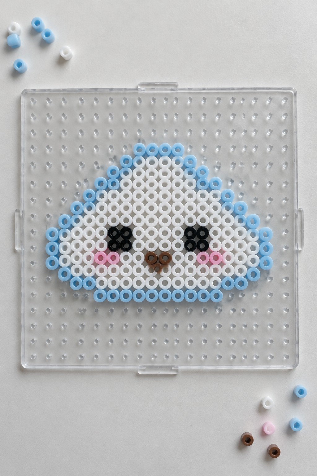 Perler beads forming a cartoon face with blue border, black eyes, and pink cheeks on pegboard.