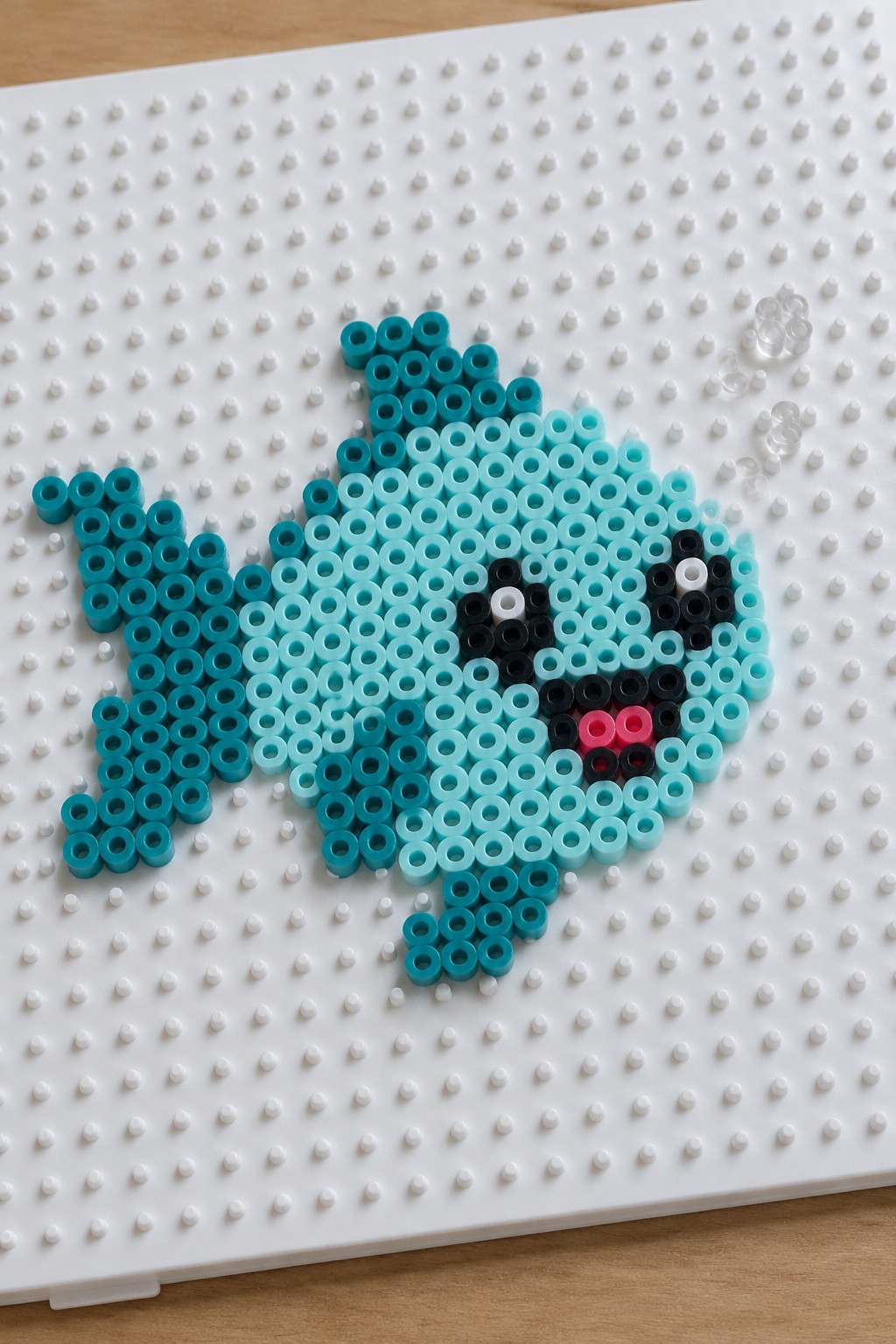 Blue perler beads forming fish with black eye and pink mouth on pegboard