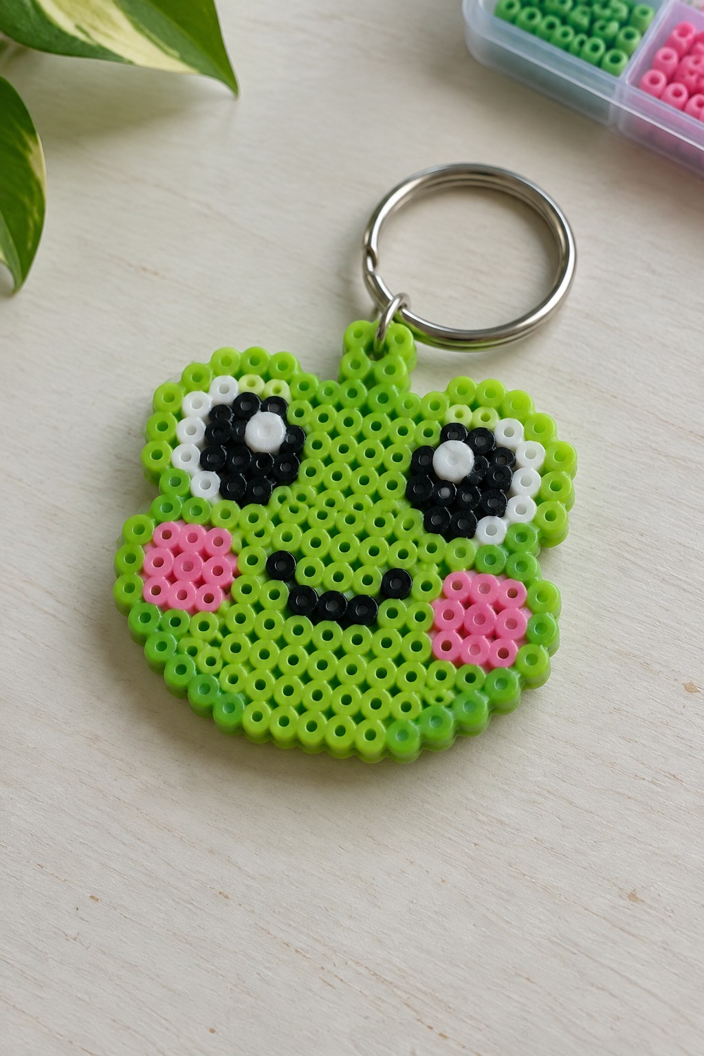 Green perler bead frog keychain with black eyes, pink cheeks, and metal ring