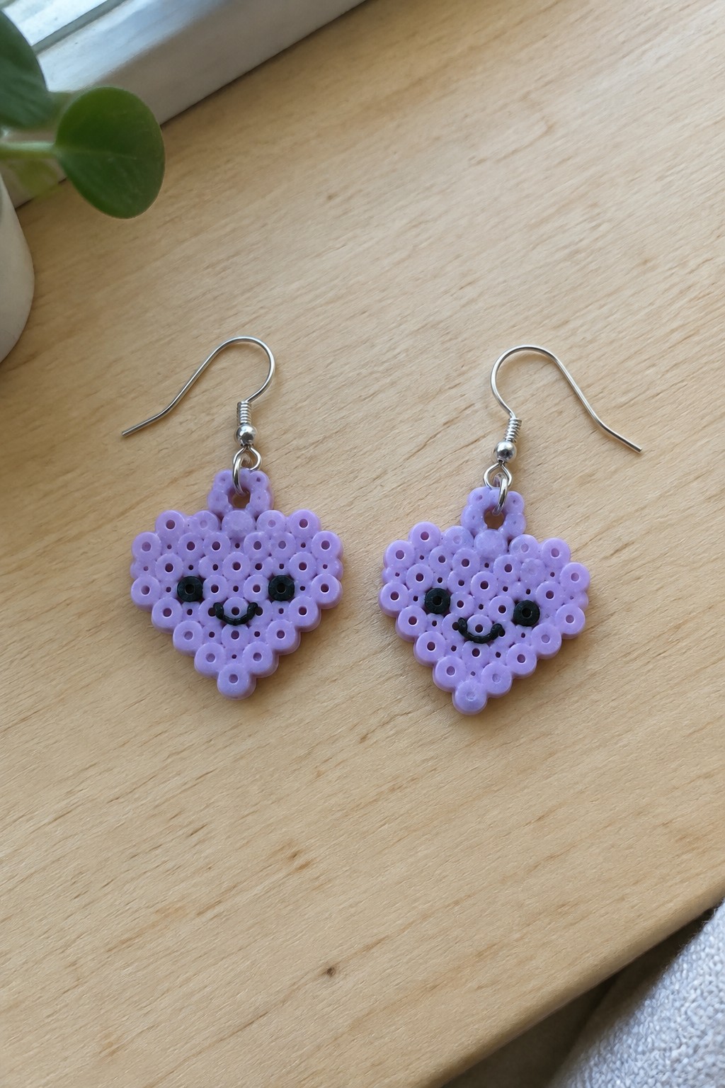 Two purple perler bead heart earrings with smiling faces on wooden table