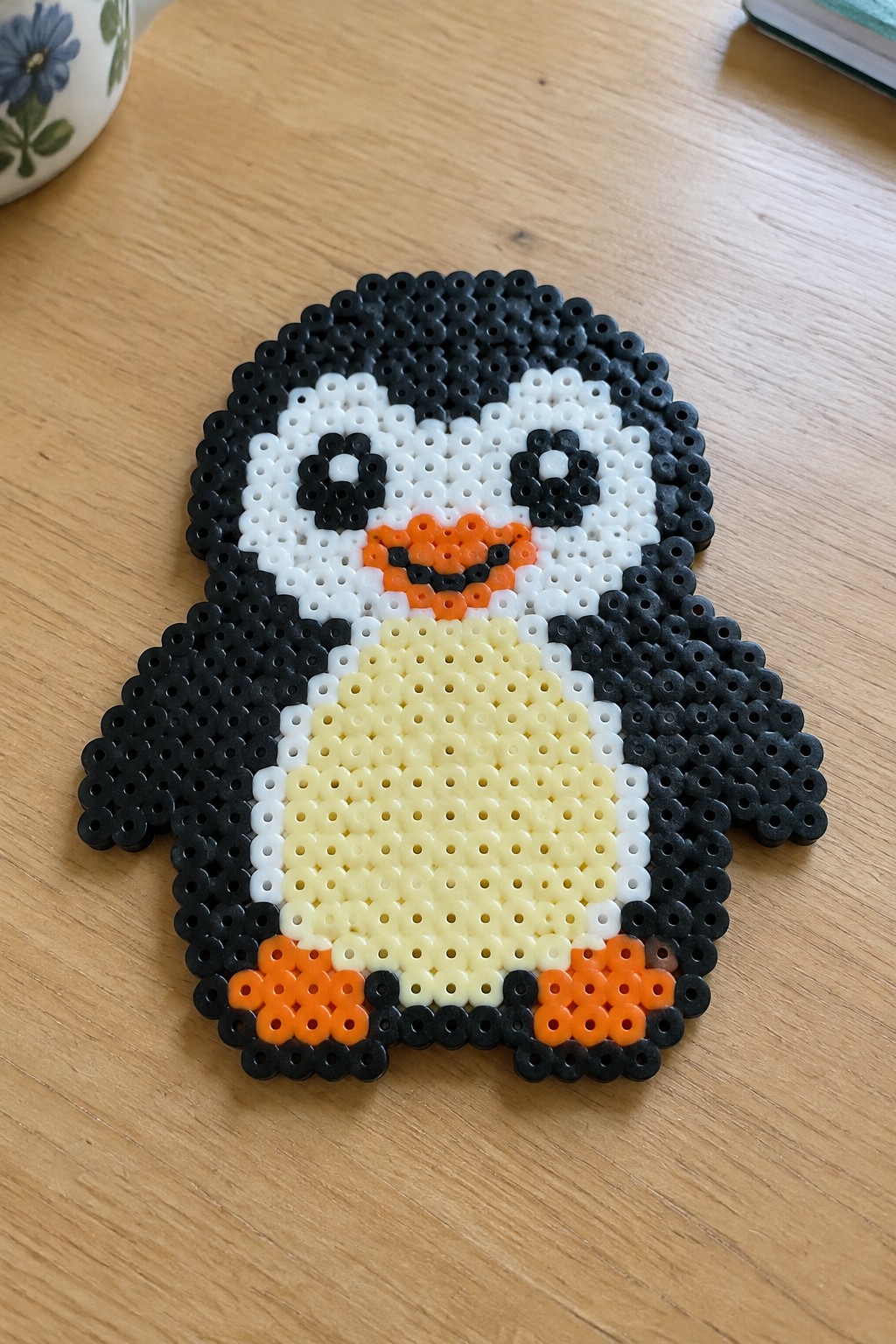 Perler bead penguin with black body, white face, yellow belly, orange beak and feet.