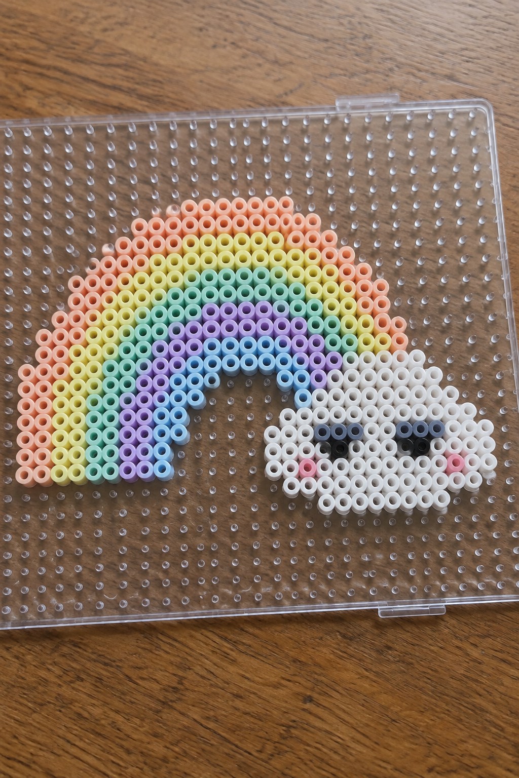 Rainbow perler beads forming an arc beside a smiling cloud face on pegboard