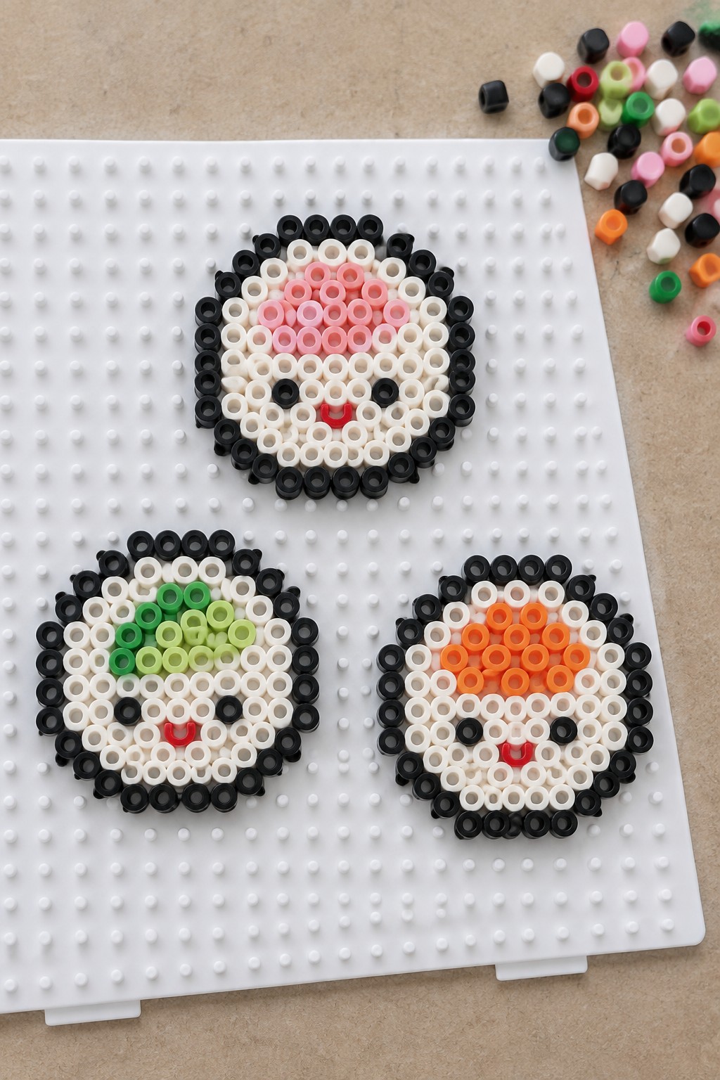 Three unfused Perler bead sushi designs with pink, green, and orange centers on a white pegboard.