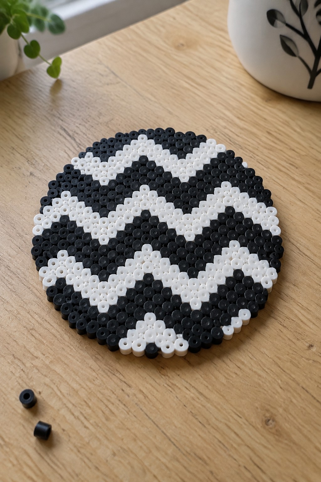 Circular black and white perler bead mat on wooden table with loose beads nearby