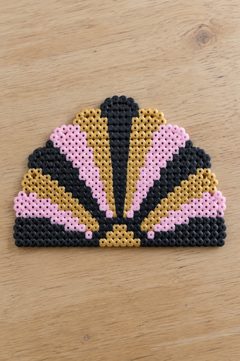 Perler bead crown design in black, pink, and gold on wooden surface