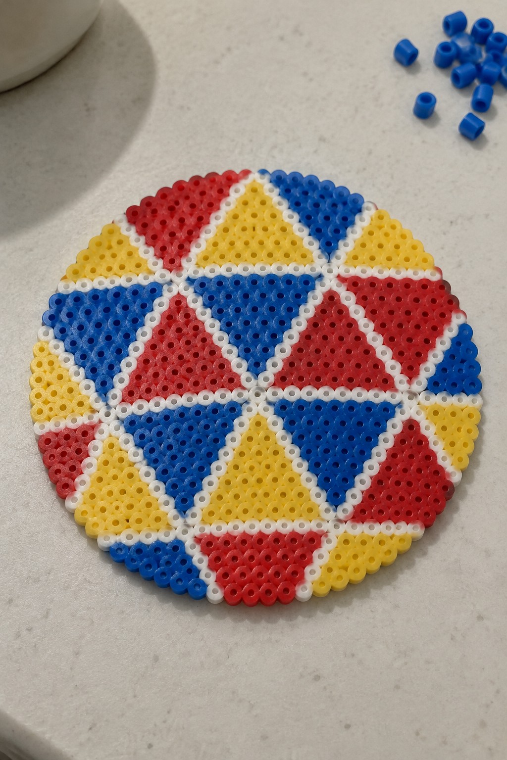 Circular Perler bead art with red, blue, yellow, white geometric triangle patterns.