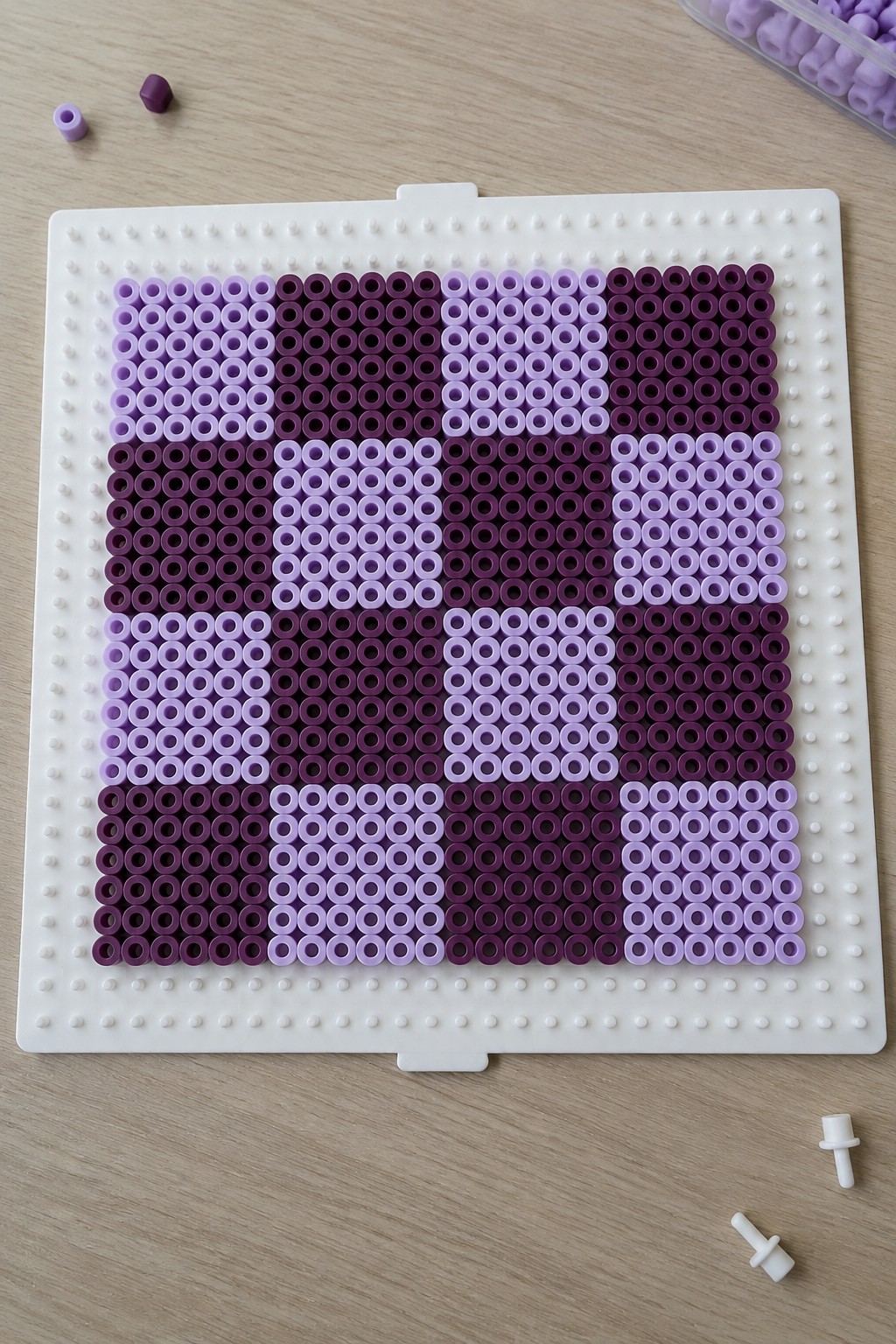 Purple and lavender beads forming pixel art on a white pegboard