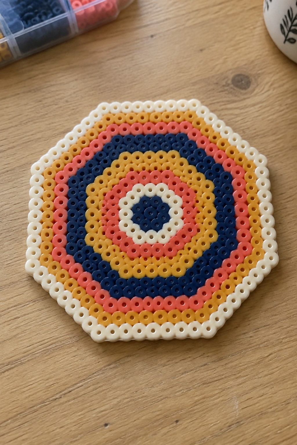 Colorful perler bead circle with concentric rings of white, yellow, pink, and blue on wood