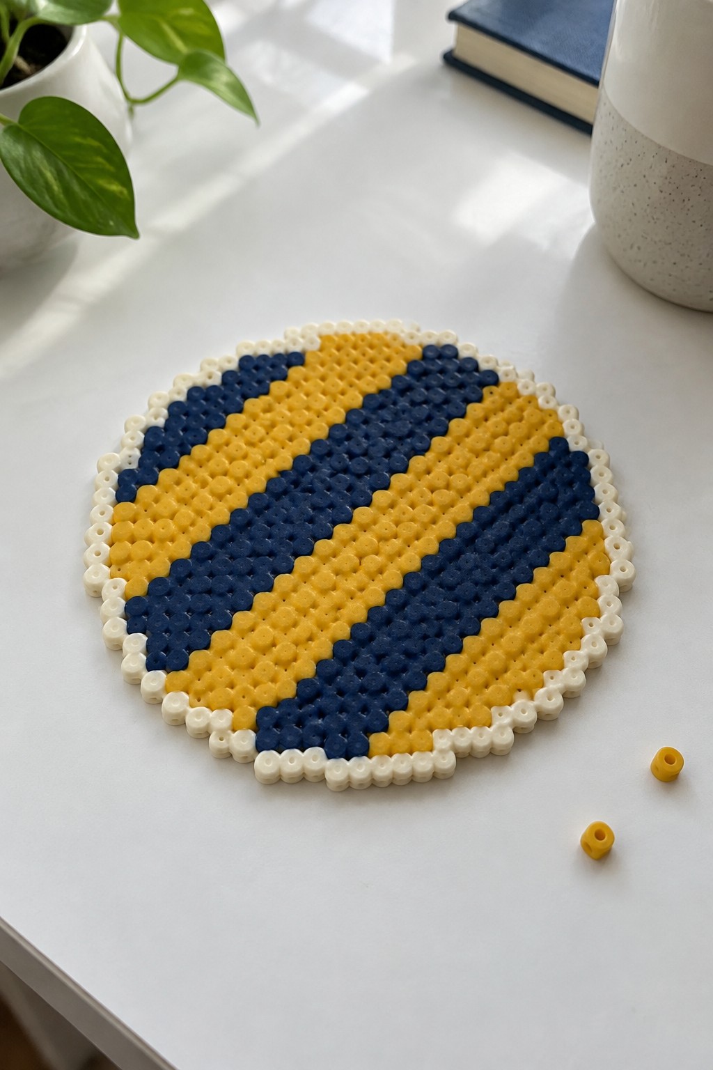 Circular perler bead art with yellow and navy diagonal stripes on white table.