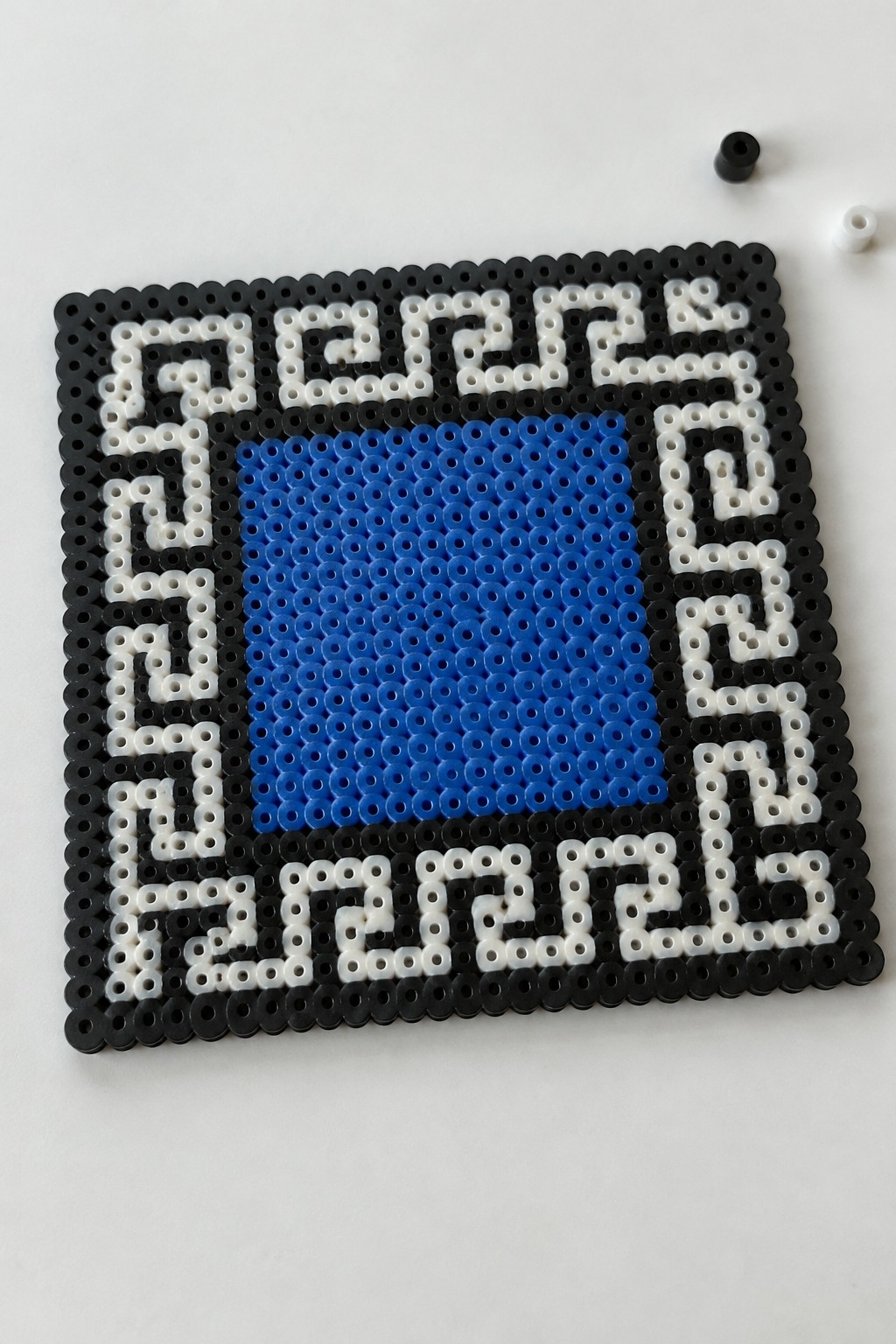 Square perler bead design spelling FUCK around solid blue center on white surface
