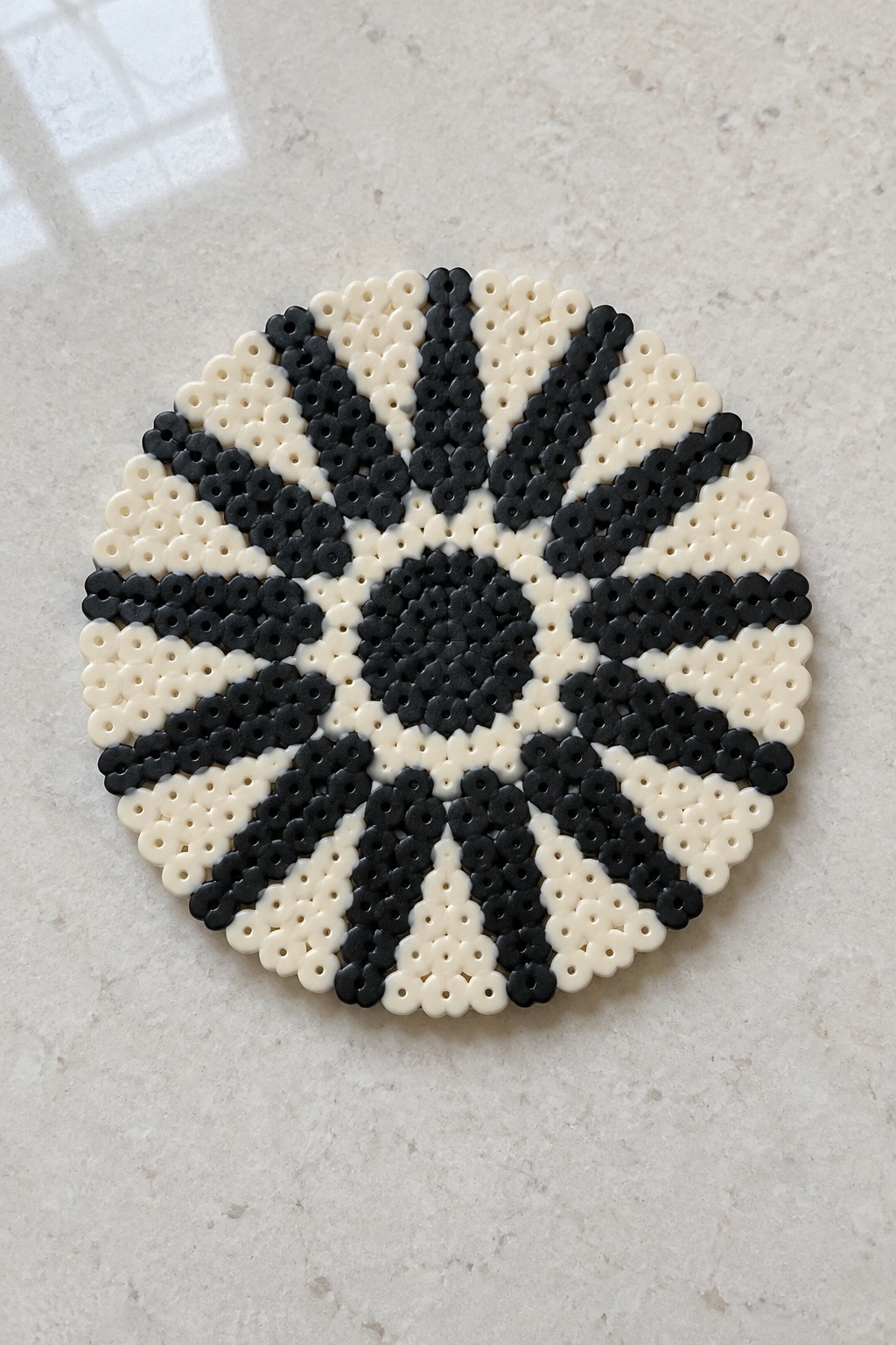 Black and white circular bead mandala with symmetrical starburst pattern on marble.