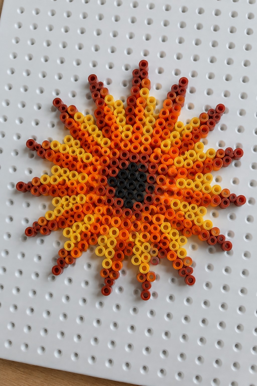 Perler bead sun with gradient red-orange-yellow rays and black center on pegboard