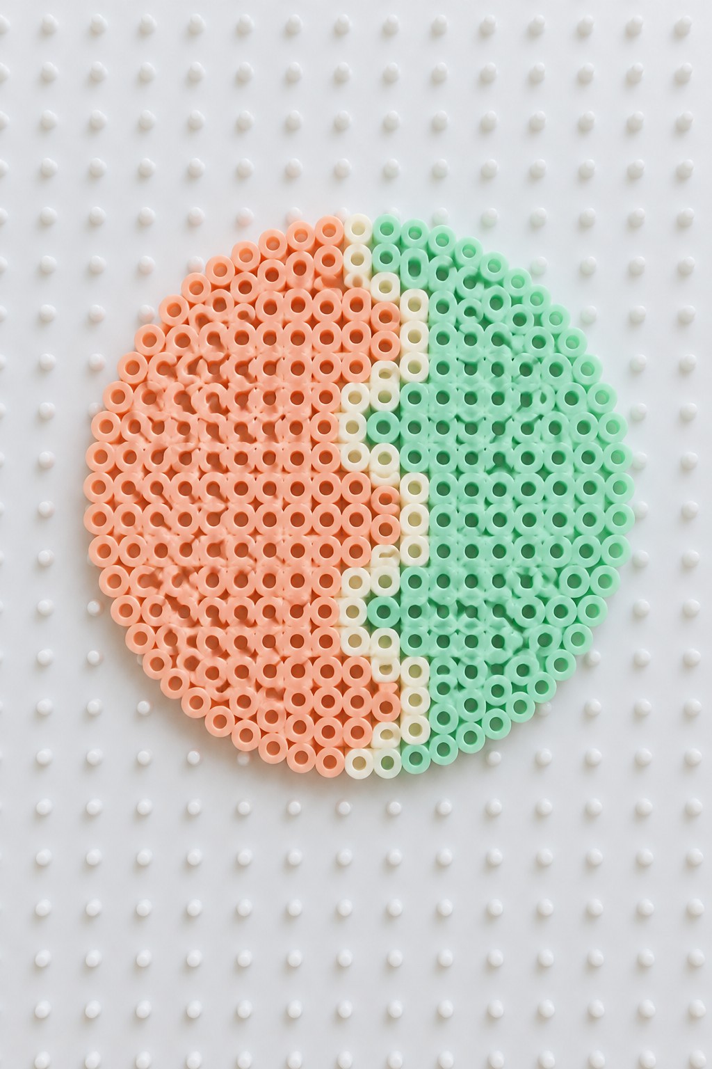 Circular perler beads in peach, white, and mint green sections on white pegboard.