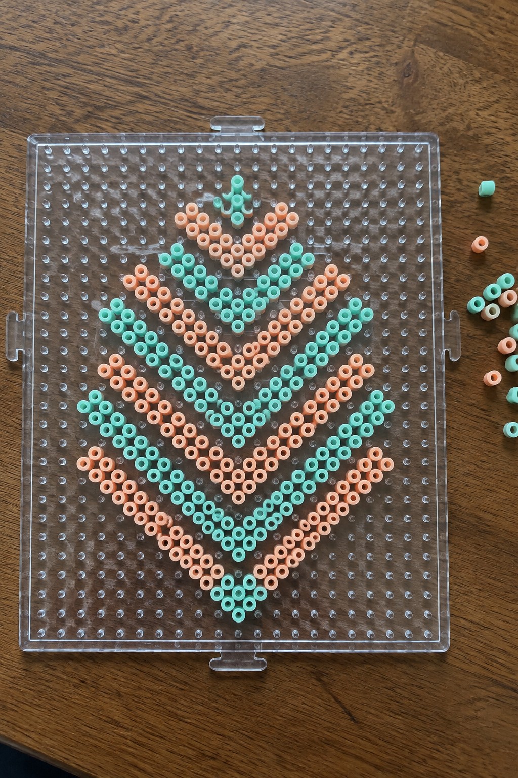 Peach and mint green beads forming a symmetrical heart design on a clear pegboard.